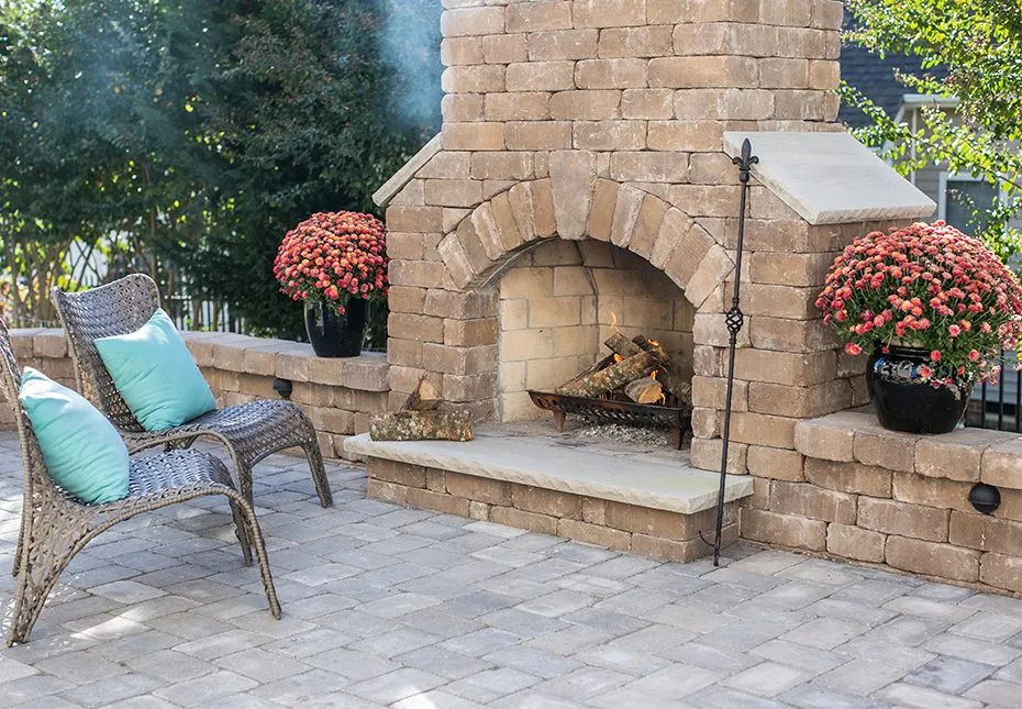 Tan stone fireplace with chairs facing it and flower pots on each side. Featured in the outdoor living inspiration gallery.